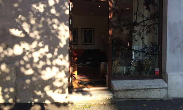 Bild på KASTELLGATAN 16 Entrén i eftermiddagssol med dörren öppen mot gatan – alldeles intill linden, strax mittemot surdegsbageriet Alvar & Ivar och med restaurangen Dubbel Dubbel runt hörnet. September 2014.